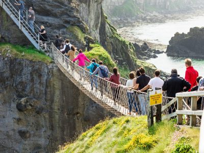 Thousands of tourists visiting Carrick-a-Rede Rope Bridge in County Antrim of Northern Ireland, hanging 30m above rocks and spanning 20m, linking mainland with the tiny island of Carrickarede
